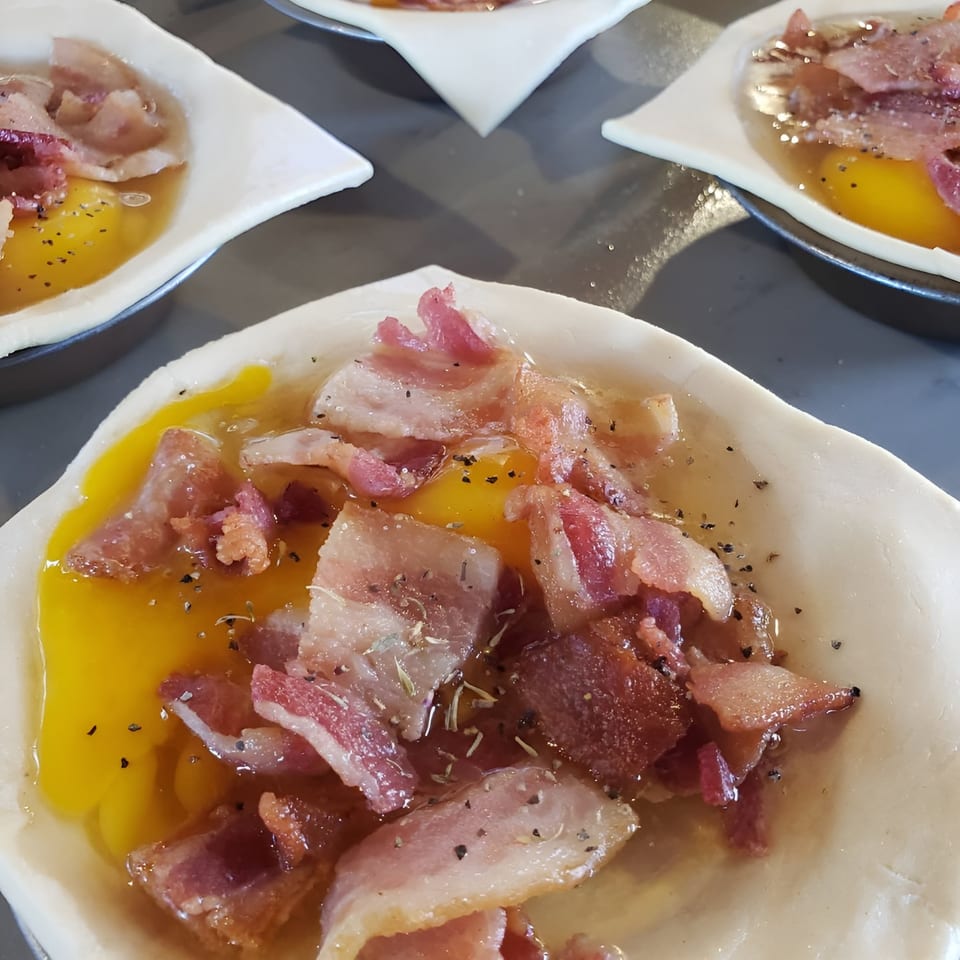 Unbaked Bula Pies with raw egg, bacon, and seasoning in a pastry shell, ready for baking.