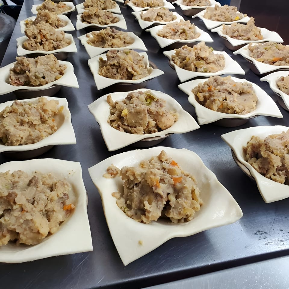 Rows of uncooked Bula Pies Fiji pastry shells filled with savory meat and vegetable filling.