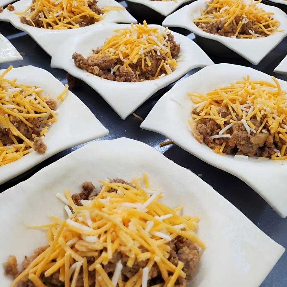 Unbaked Bula Pies with savory filling and shredded cheese, ready for the oven.